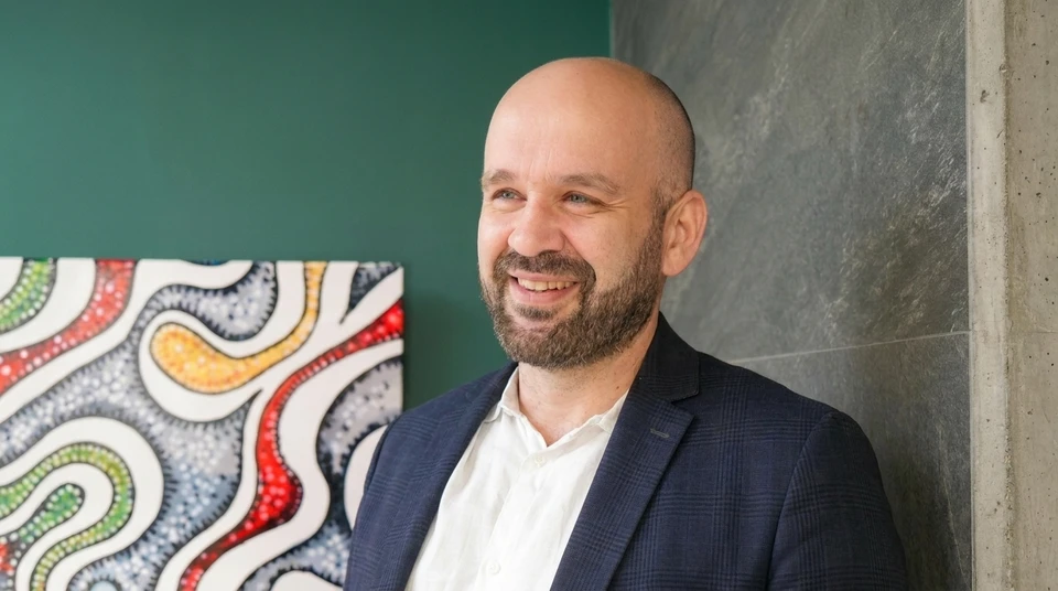 Un professionnel en agencement intérieur (apparence soignée, vêtu professionnellement) présenté dans un showroom moderne et lumineux, en train de discuter avec un client devant des plans ou des échantillons de matériaux (carrelage, revêtements). L'interaction montre une écoute active et un accompagnement personnalisé. La scène capture le moment de la relation client premium et du conseil en conception, illustrant la continuité et la cohérence du suivi. Arrière-plan professionnel montrant des éléments d'agencement (cuisine design, rangements sur mesure, salles de bain).